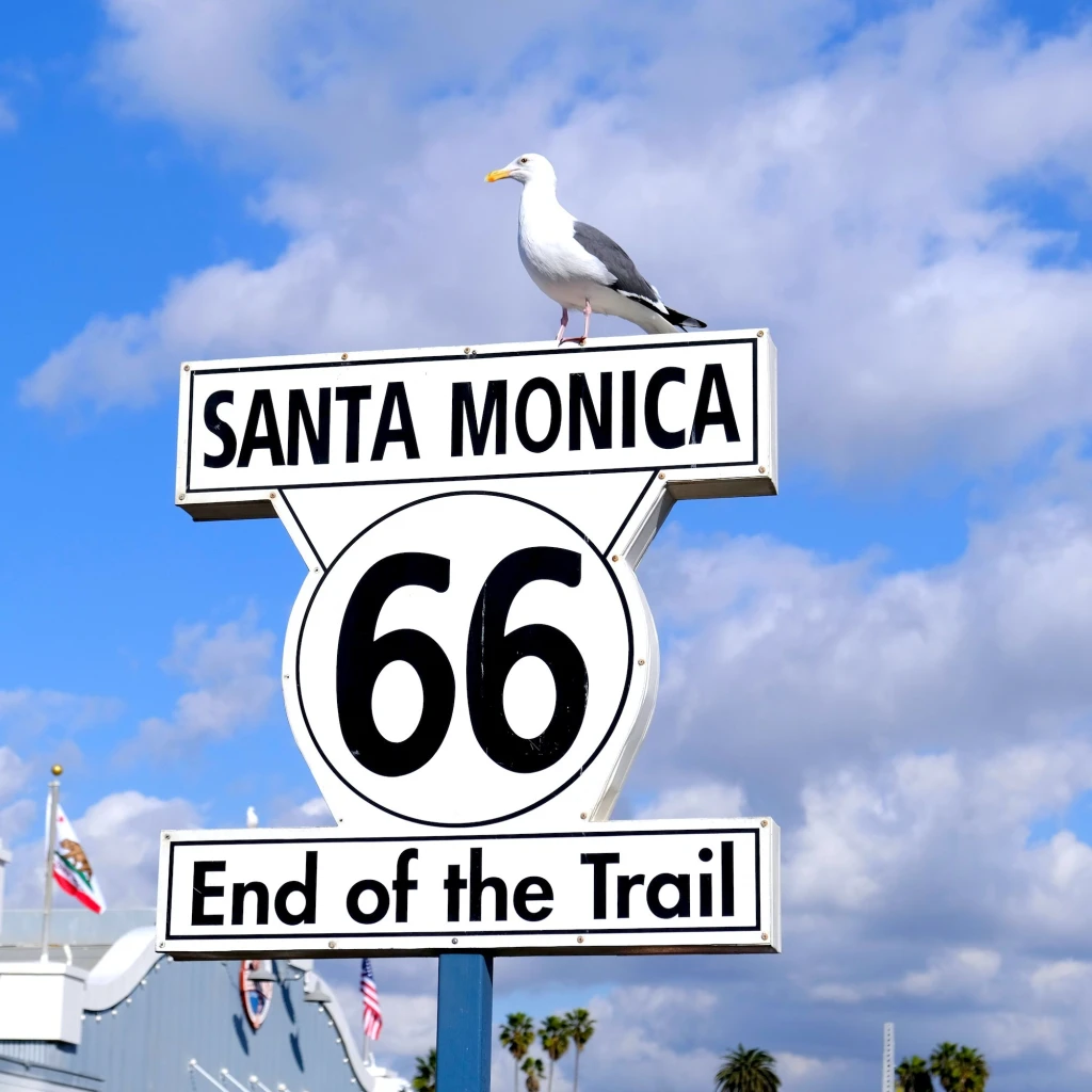 Het Route 66 bord "End of the Trail" in Santa Monica, VS, met een meeuw bovenop tegen een felblauwe lucht.