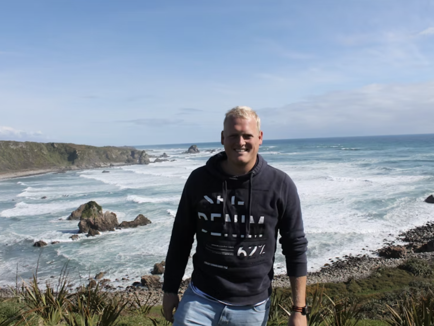 Maurits glimlacht naar de camera met de oceaan op de achtergrond