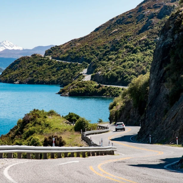 Een auto rijdt naast een blauw meer tussen de bergen in Nieuw-Zeeland