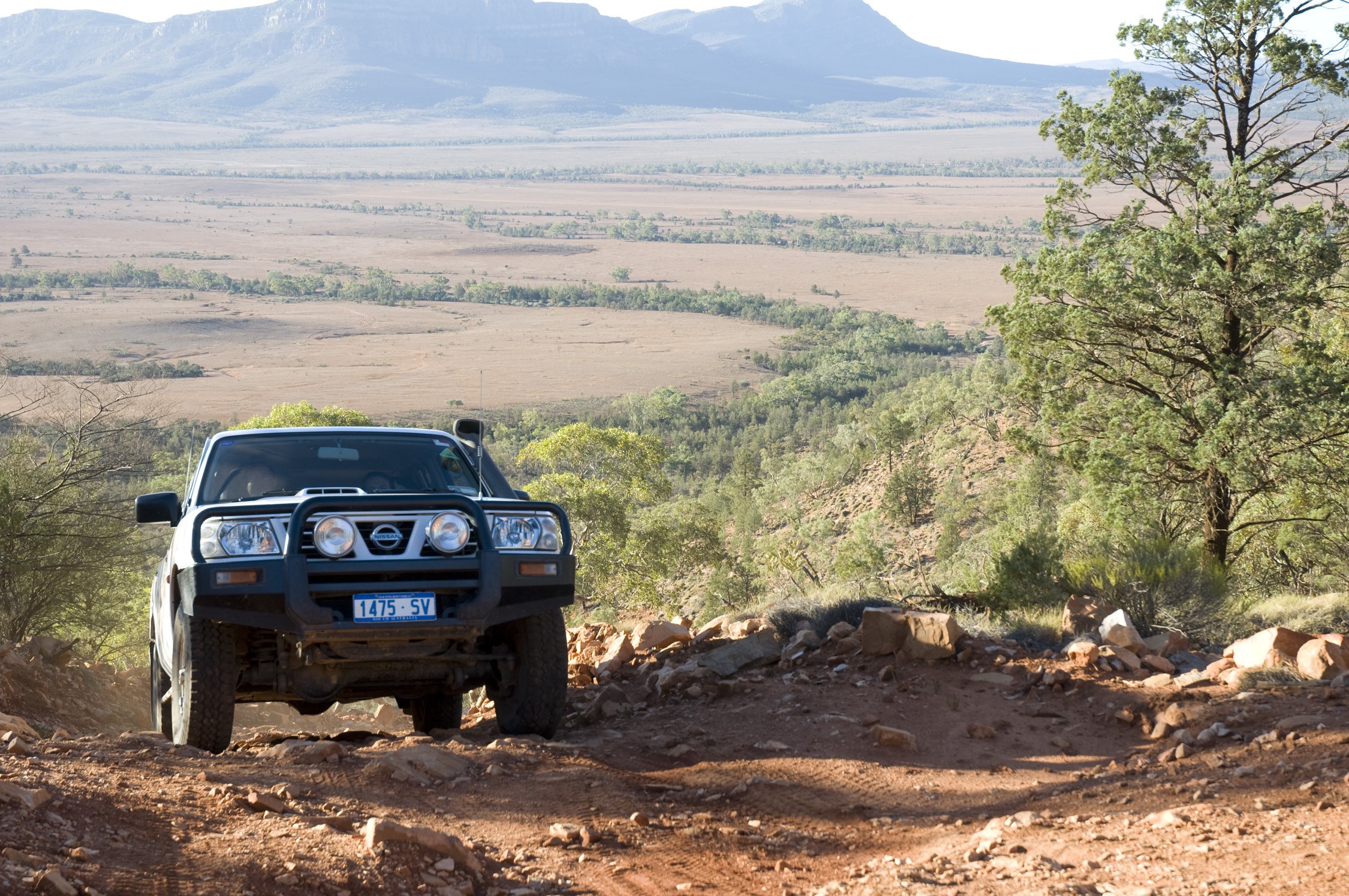 4WD auto rijdt op een bergopwaarts zandpad met velden en bergen op de achtergrond