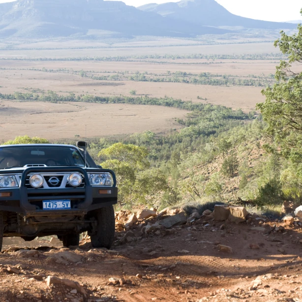 4WD auto rijdt op een bergopwaarts zandpad met velden en bergen op de achtergrond
