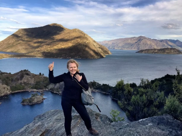 Gerrie glimlacht en geeft een duim omhoog naar de camera met de oceanen en bergen op de achtergrond