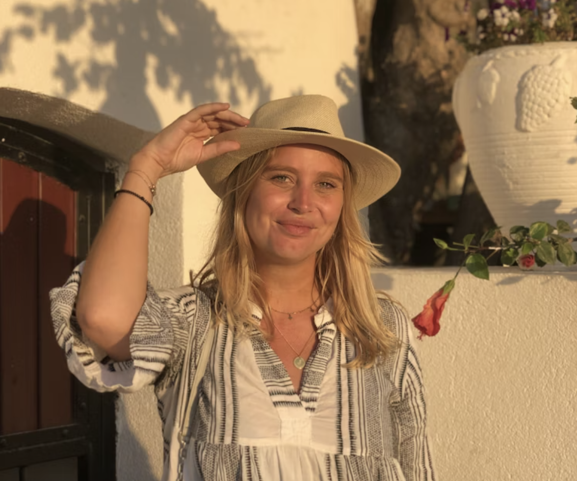 Juna glimlacht naar de camera terwijl ze haar hoed vasthoudt