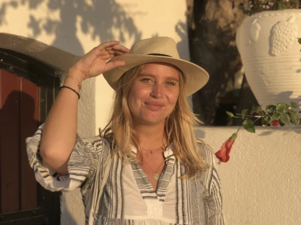 Juna glimlacht naar de camera terwijl ze haar hoed vasthoudt