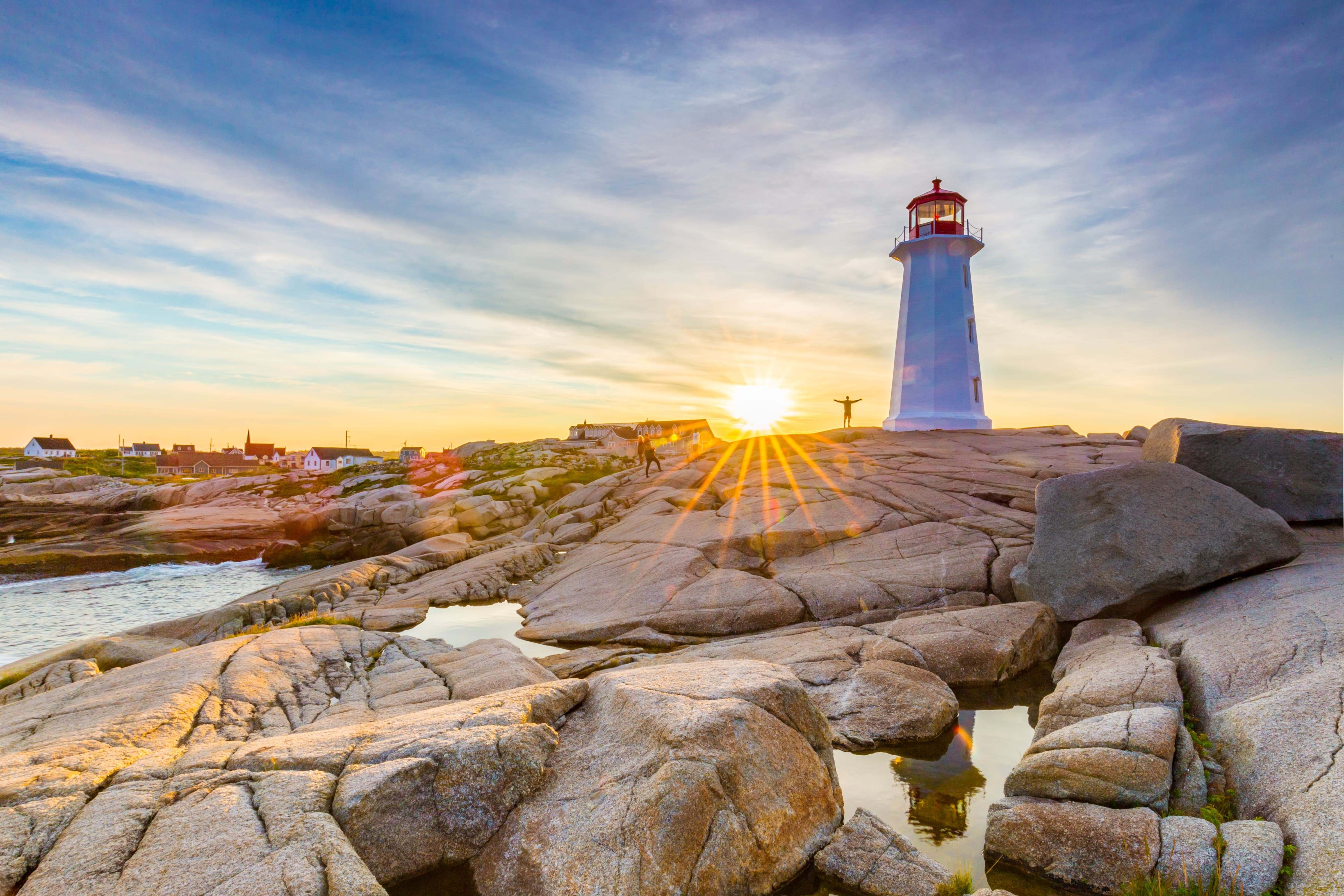 Een vuurtoren staat op de rotsen, met de ondergaande zon op de achtergrond, in Peggy's Cove, in het oostelijke deel van Canada