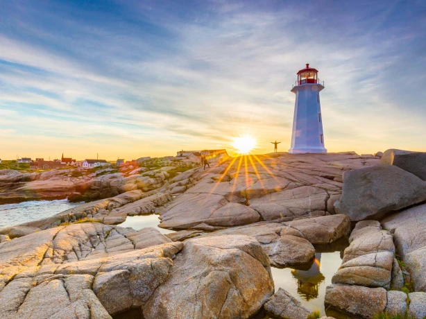 Een vuurtoren staat op de rotsen, met de ondergaande zon op de achtergrond, in Peggy's Cove, in het oostelijke deel van Canada