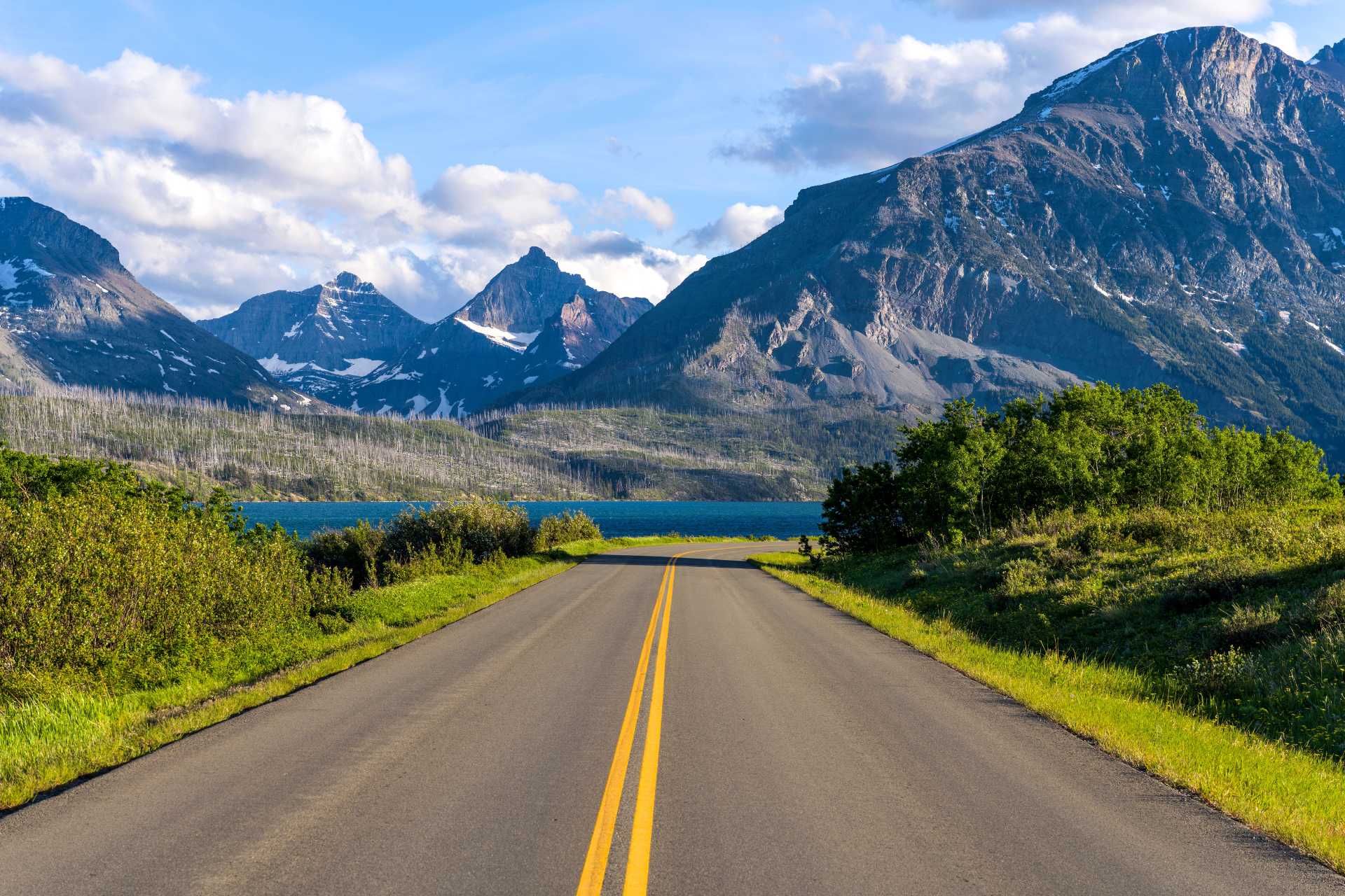 Een open weg die leidt naar de bergen en het meer in Glacier National Park, Montana, VS, onder een heldere zomerhemel.