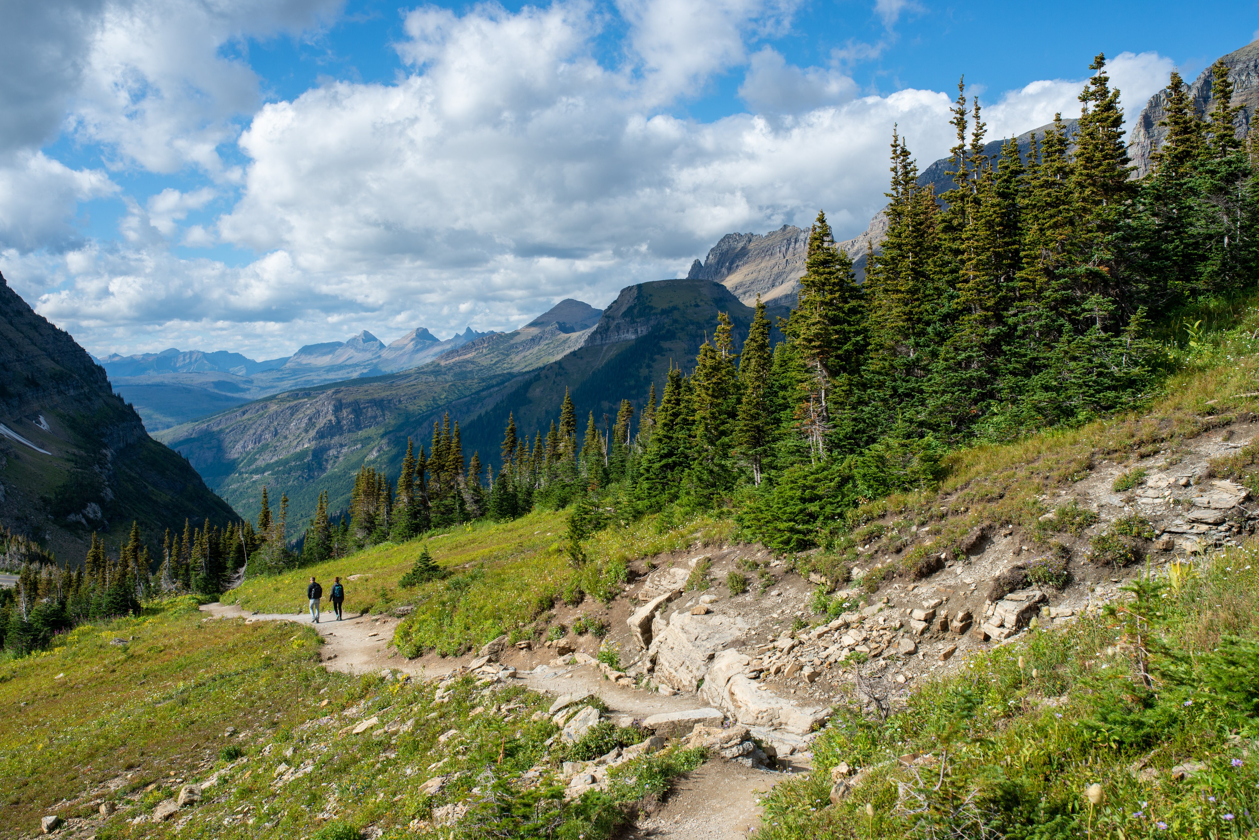 Couple hiking trail surrounded by mountains in Glacier National Park