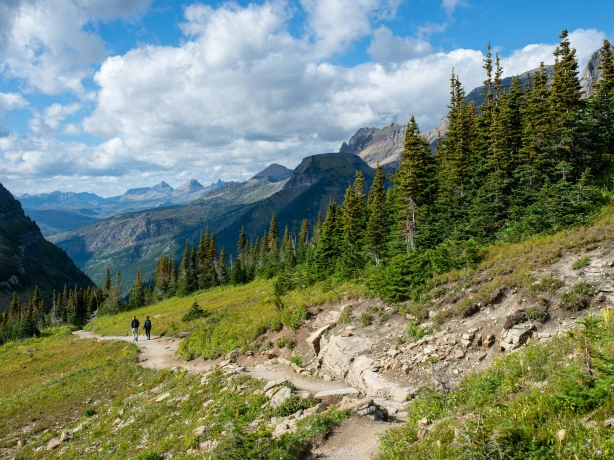 Couple hiking trail surrounded by mountains in Glacier National Park