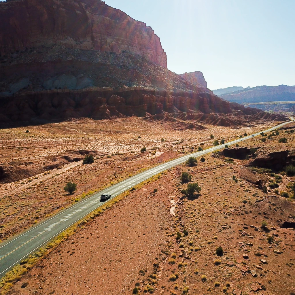 Een auto rijdt over een afgelegen woestijnweg in Utah, omringd door rode rotskliffen en weidse landschappen.