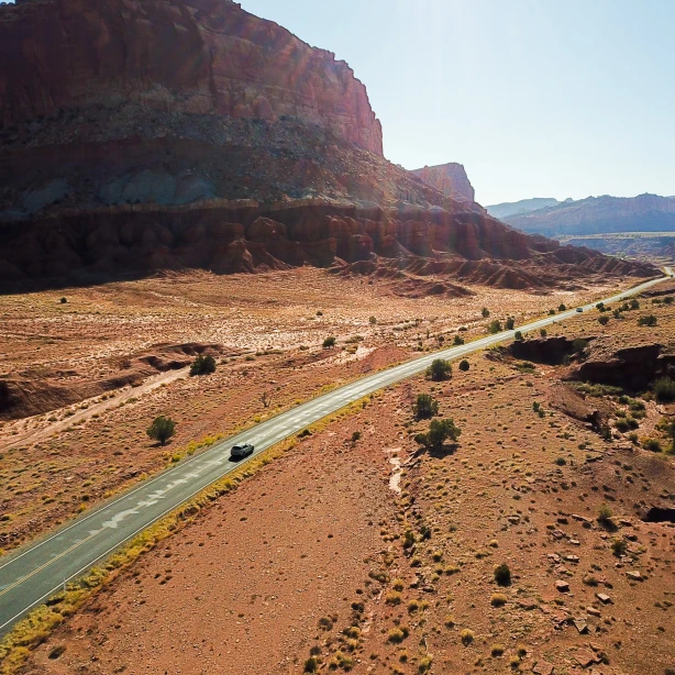 Een auto rijdt over een afgelegen woestijnweg in Utah, omringd door rode rotskliffen en weidse landschappen.