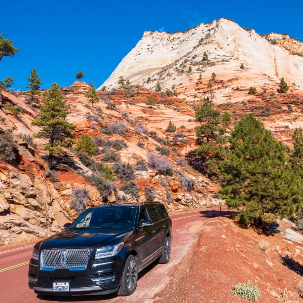Een zwarte SUV geparkeerd langs een kronkelende woestijnweg in het zuidwesten van de Verenigde Staten, met opvallende rode en witte zandstenen kliffen die oprijzen onder een strakblauwe hemel.