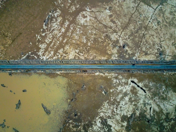 Een rechte weg dwars door de dorre woestijnvlakte van Death Valley, van bovenaf gezien met waterpartijen en gebarsten aarde aan weerszijden.