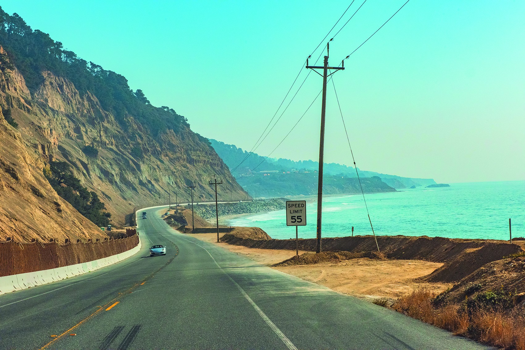 Een kustweg in Californië die buigt langs steile kliffen boven de oceaan, met auto's die langs het turquoise water rijden.