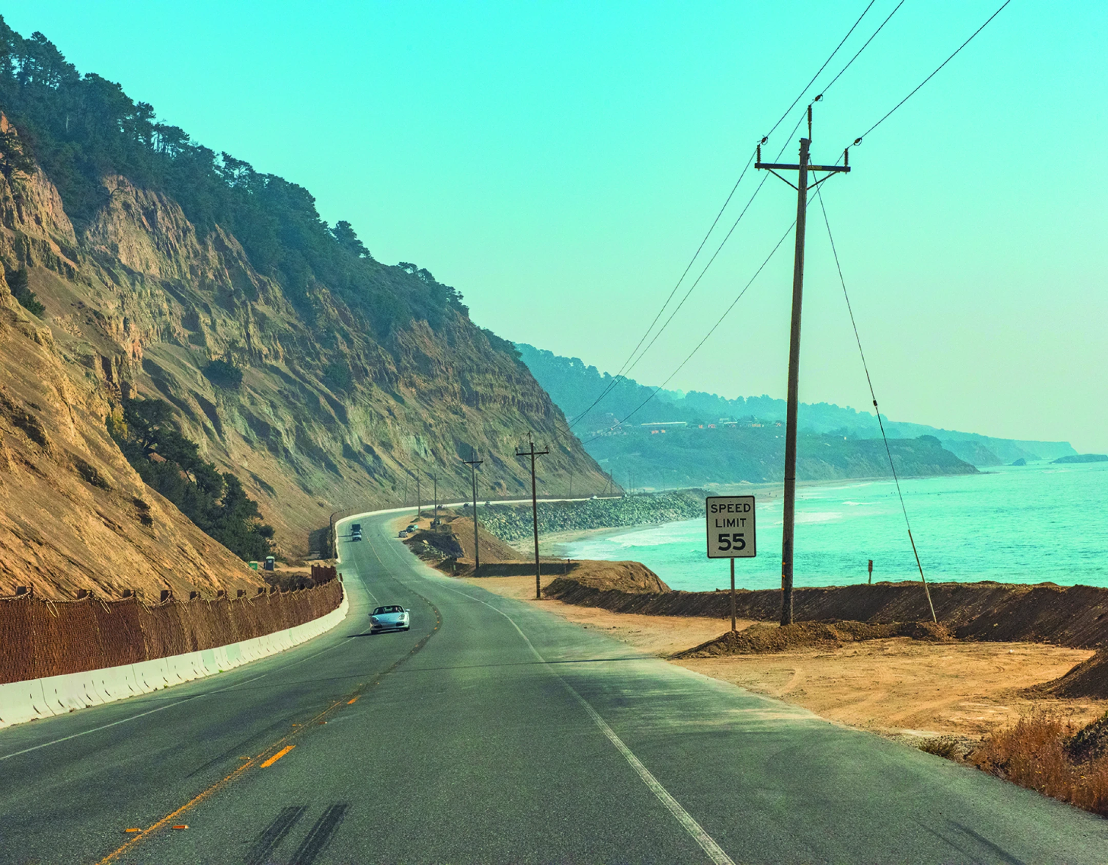 Een kustweg in Californië die buigt langs steile kliffen boven de oceaan, met auto's die langs het turquoise water rijden.