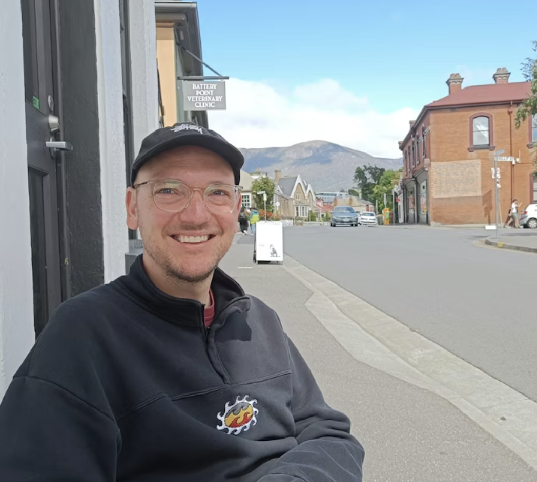 Sjoerd lacht naar de camera met een stad en bergen op de achtergrond