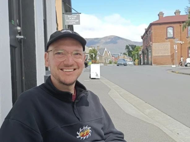 Sjoerd lacht naar de camera met een stad en bergen op de achtergrond