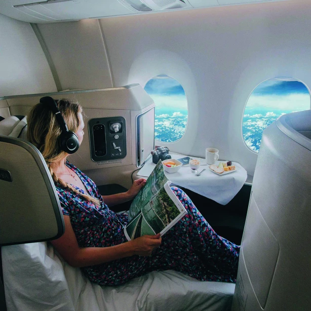 Een vrouw met een koptelefoon op leest een tijdschrift in de Business Class van een vliegtuig