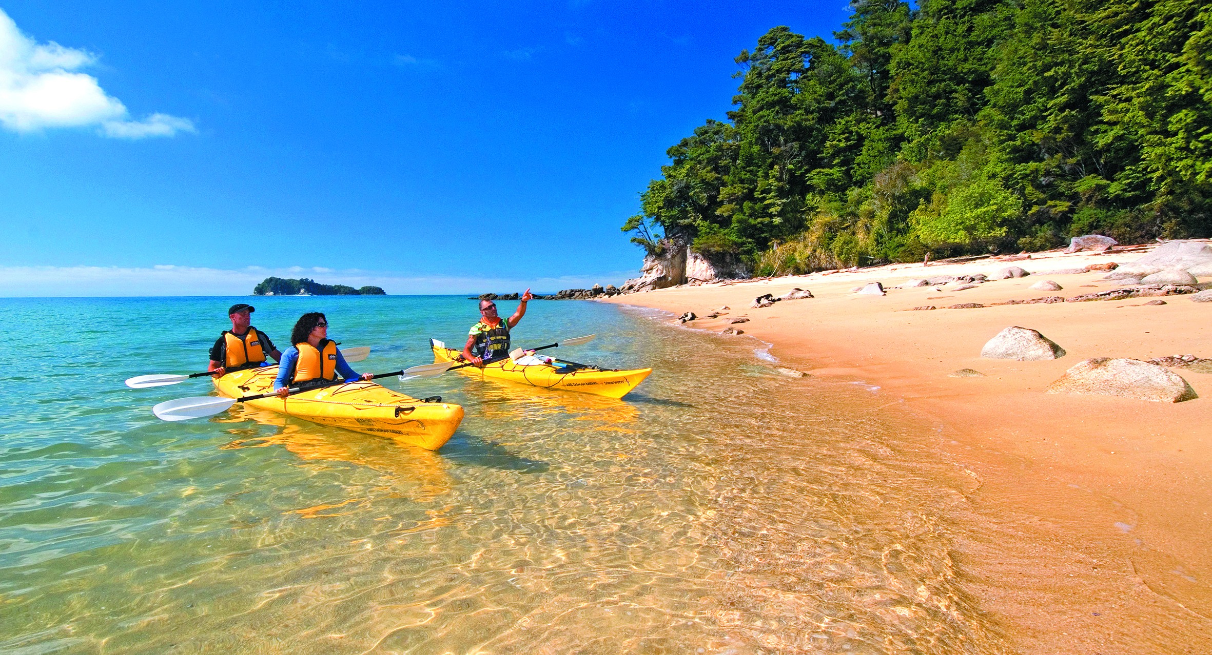 Drie mensen kajakken op zee langs de kust in Abel Tasman