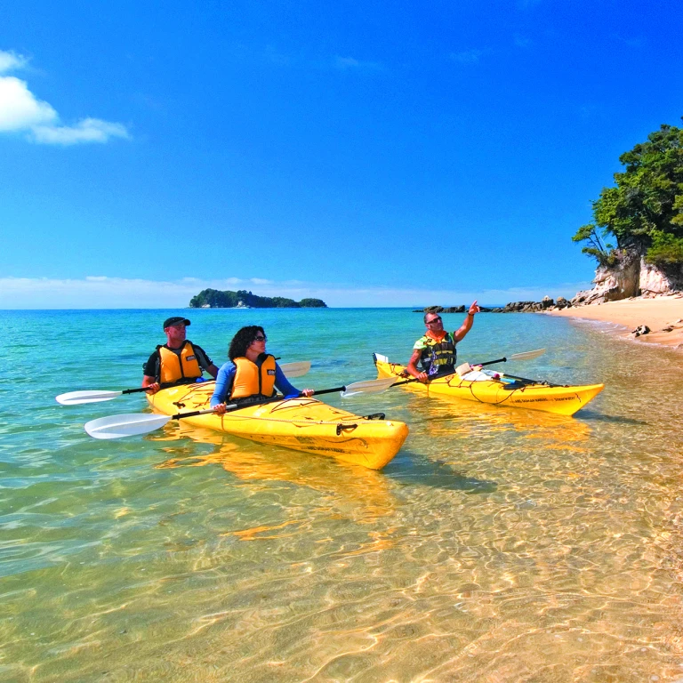 Drie mensen kajakken op zee langs de kust in Abel Tasman