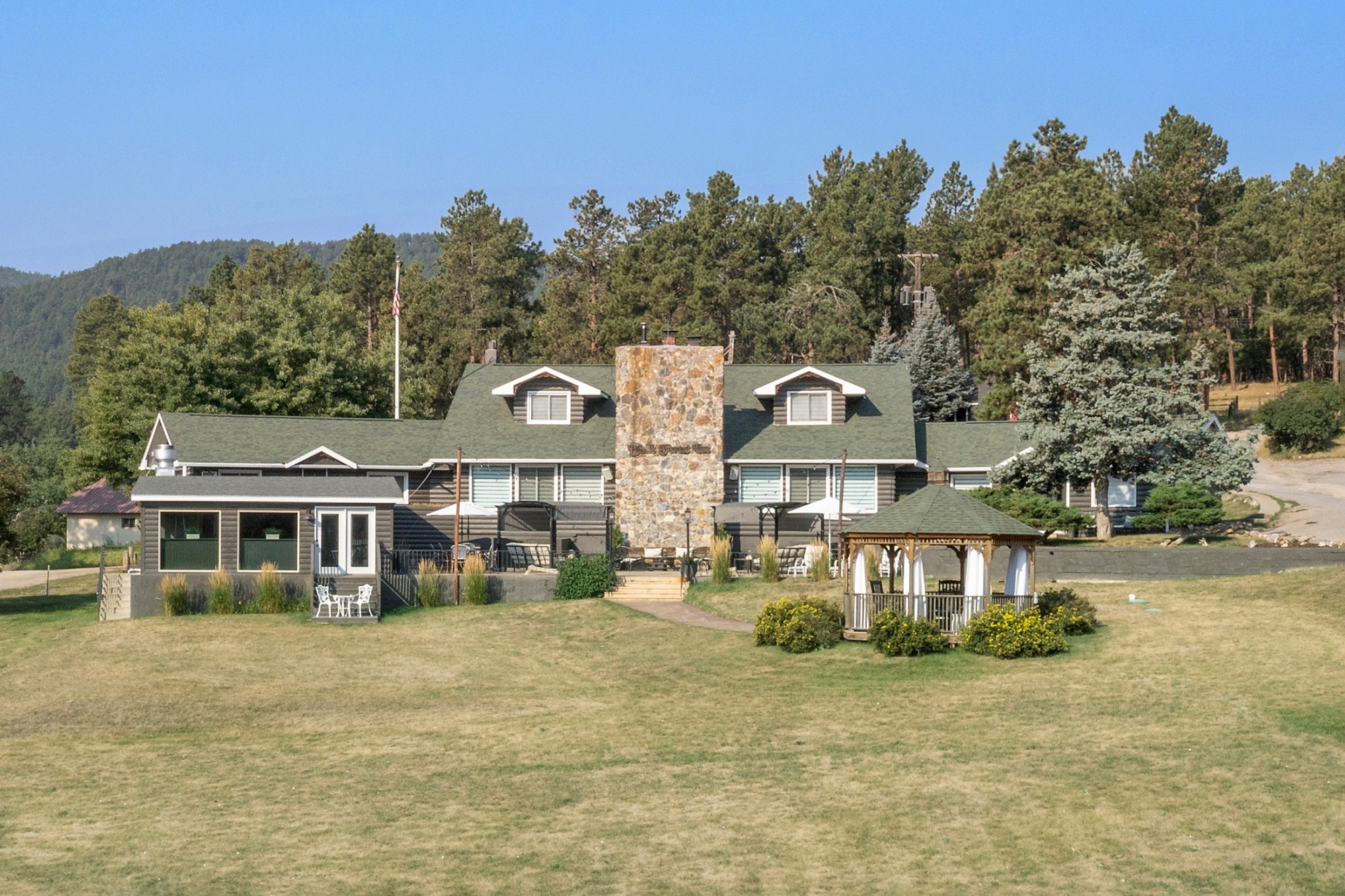 Rustieke blokhut met een hoge stenen schoorsteen en een prieel op een open grasveld, omgeven door met dennenbomen begroeide heuvels in de Black Hills-regio in South Dakota, VS.