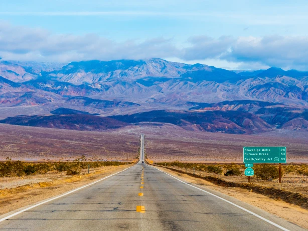 Een lange rechte weg die zich uitstrekt door de Mojavewoestijn van Californië naar de bergen van Death Valley, met woestijnvlakten en bergkammen in de verte onder een heldere hemel.