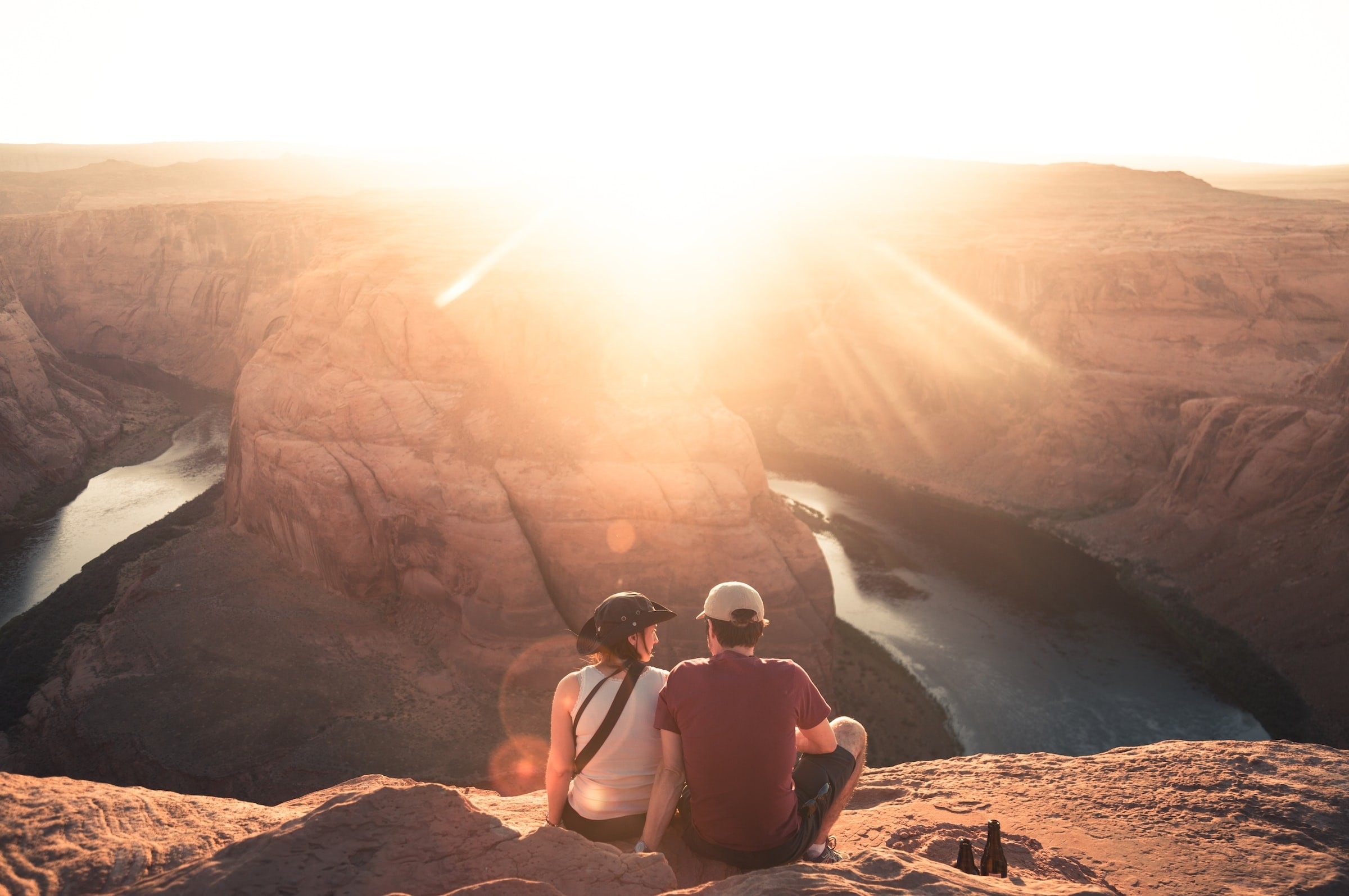 Een stel zit met uitzicht op Horseshoe Bend in Moab, Arizona, terwijl de zon fel in de lens schijnt.
