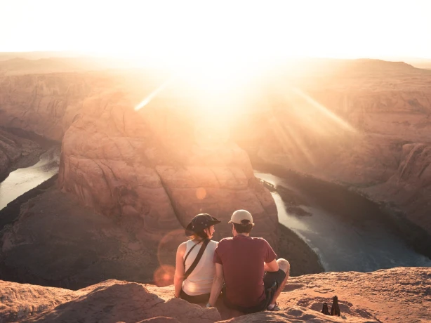 Een stel zit met uitzicht op Horseshoe Bend in Moab, Arizona, terwijl de zon fel in de lens schijnt.