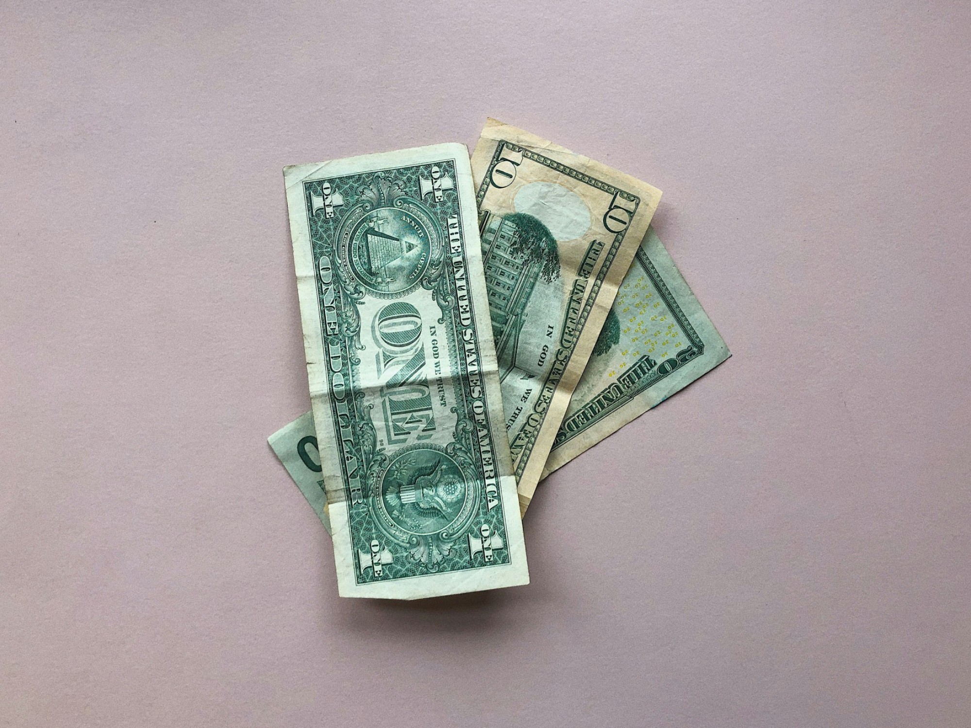 Een klein stapeltje Amerikaanse dollarbiljetten op een lichtroze oppervlak.