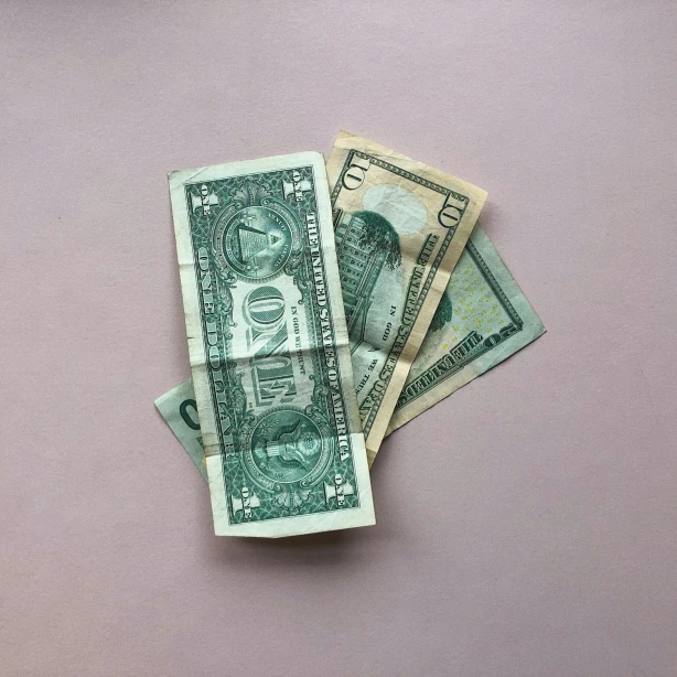 Een klein stapeltje Amerikaanse dollarbiljetten op een lichtroze oppervlak.