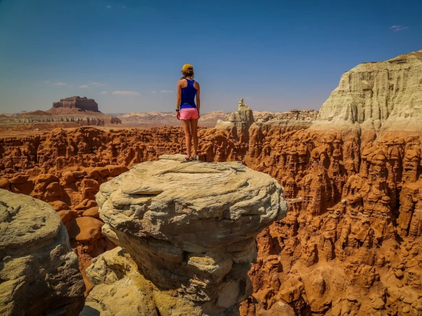 Een wandelaar staat op een rotsrichel met uitzicht op de gebeeldhouwde rode rotsformaties en het woestijnlandschap van het Amerikaanse zuidwesten.